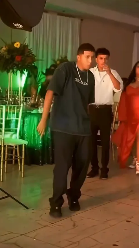 A young man in a dark oversized T-shirt and chain biting a concha at a quinceañera party